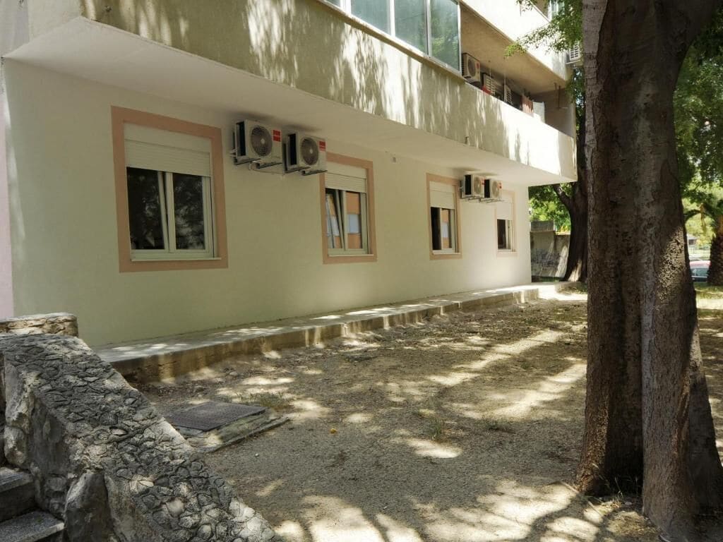 Un edificio con varias ventanas, unidades de aire acondicionado y un muro de piedra.