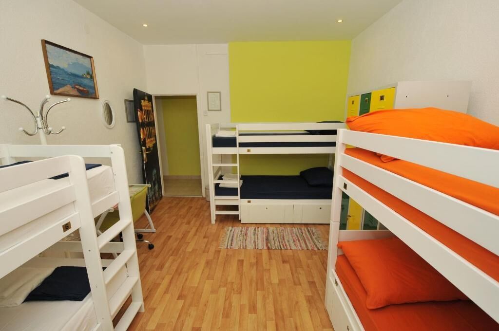 Een slaapkamer met een stapelbed, houten vloer, een schilderij aan de muur en een deur naar een andere kamer.