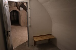 Ein schmaler Flur mit einer Bank, einer Tür zu einem Raum und einer Wand mit strukturierter Oberfläche.