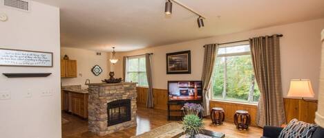 A living room with a stone fireplace, wooden flooring, a sofa, a coffee table, and a television.