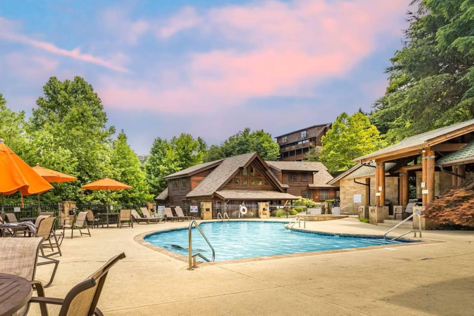 A pool area with lounge chairs, umbrellas, and a wooden building with a sloped roof.