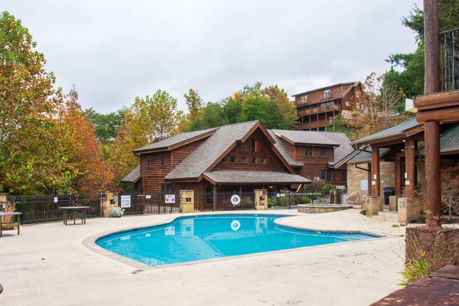 A log cabin-style building with a pool, surrounded by trees and a fence.