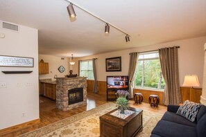 A living room with a stone fireplace, wooden flooring, a sofa, a coffee table, and a television. - Golf View Escape (Pigeon Forge)