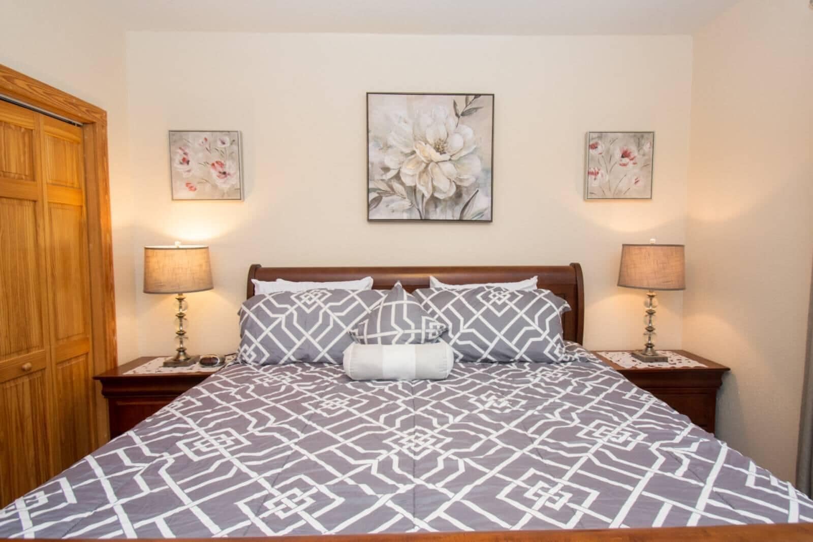 Una cama con una colcha de diseño geométrico, dos lámparas de noche y tres cuadros florales en la pared.