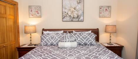 Una cama con una colcha de diseño geométrico, dos lámparas de noche y tres cuadros florales en la pared.