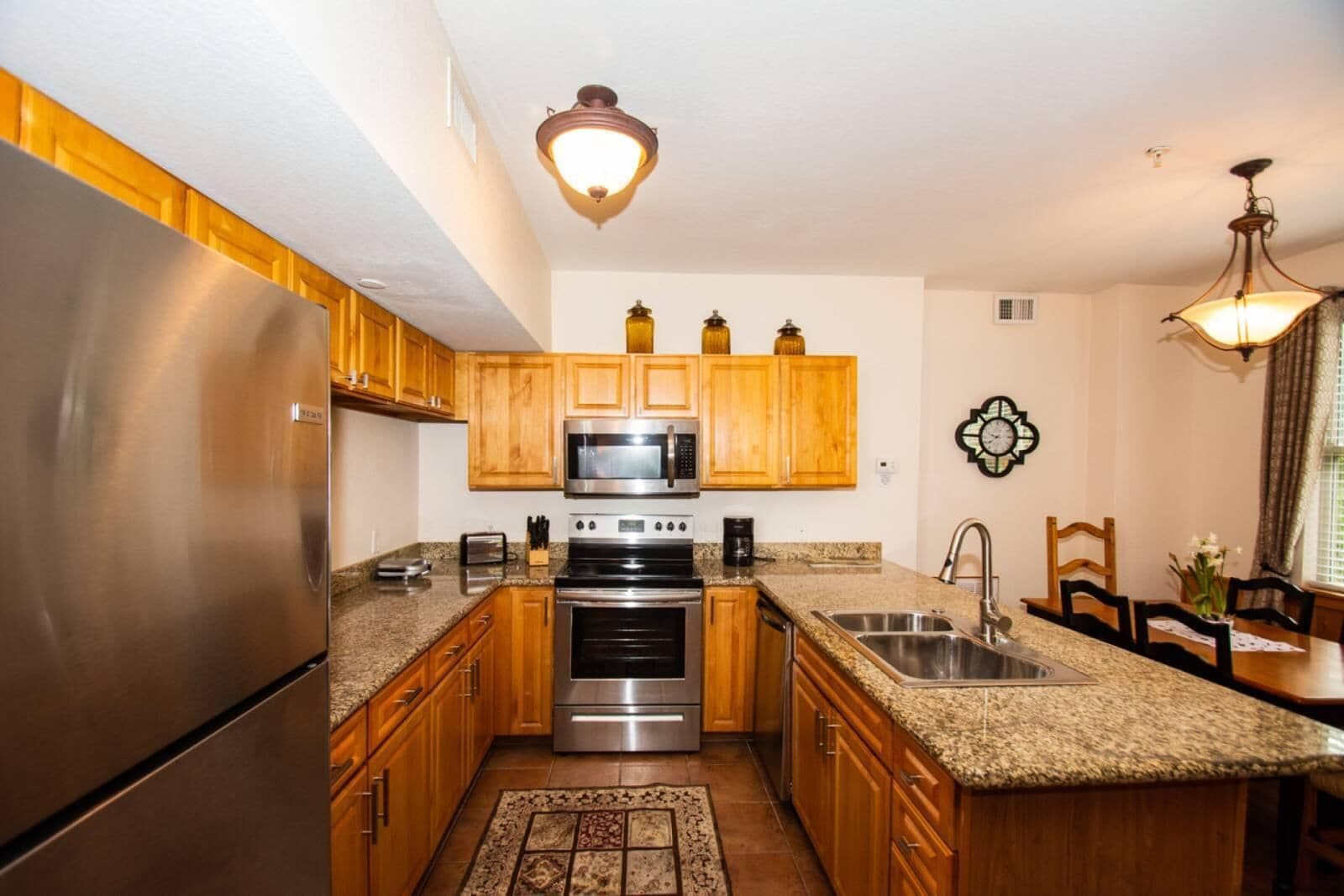 A compact kitchen with wooden cabinets, stainless steel appliances, granite countertops, and a patterned rug.
