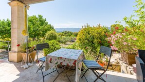 Eine Terrasse im Freien mit Tisch und Stühlen, umgeben von viel Grün und Blick auf ferne Hügel.