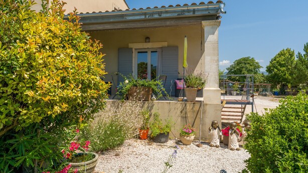 Ein Haus mit einer Veranda, Topfpflanzen und einer kleinen Statue.