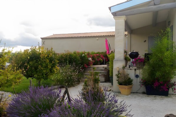 A garden with various plants and flowers, a pergola, and a building with a tiled roof.