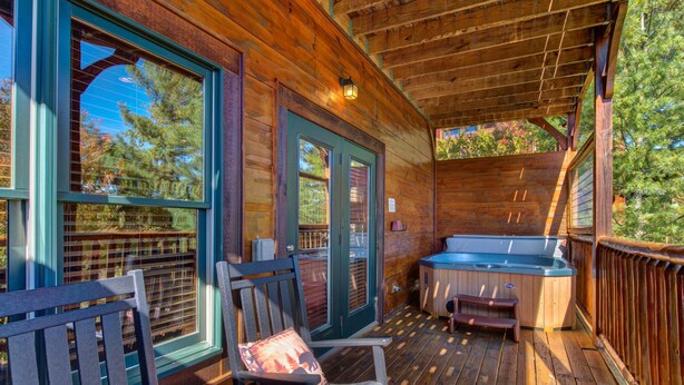 A wooden deck with a hot tub, two rocking chairs, and a door with a window. - Morning Glory (Gatlinburg)