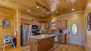 A wooden cabin interior with a kitchen featuring a central island, wooden cabinets, and a refrigerator. - Morning Glory (Gatlinburg)