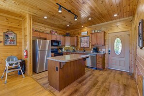 Ein Holzblockhaus-Interieur mit einer Küche, die eine zentrale Kochinsel, Holzschränke und einen Kühlschrank beinhaltet.