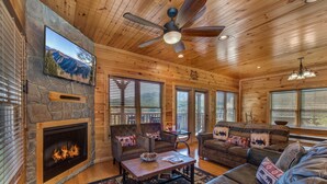 A log cabin interior with a stone fireplace, wooden ceiling, and a large window overlooking mountains. - Morning Glory (Gatlinburg)