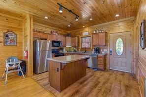 Ein Holzblockhaus-Interieur mit einer Küche, die eine zentrale Kochinsel, Holzschränke und einen Kühlschrank beinhaltet.