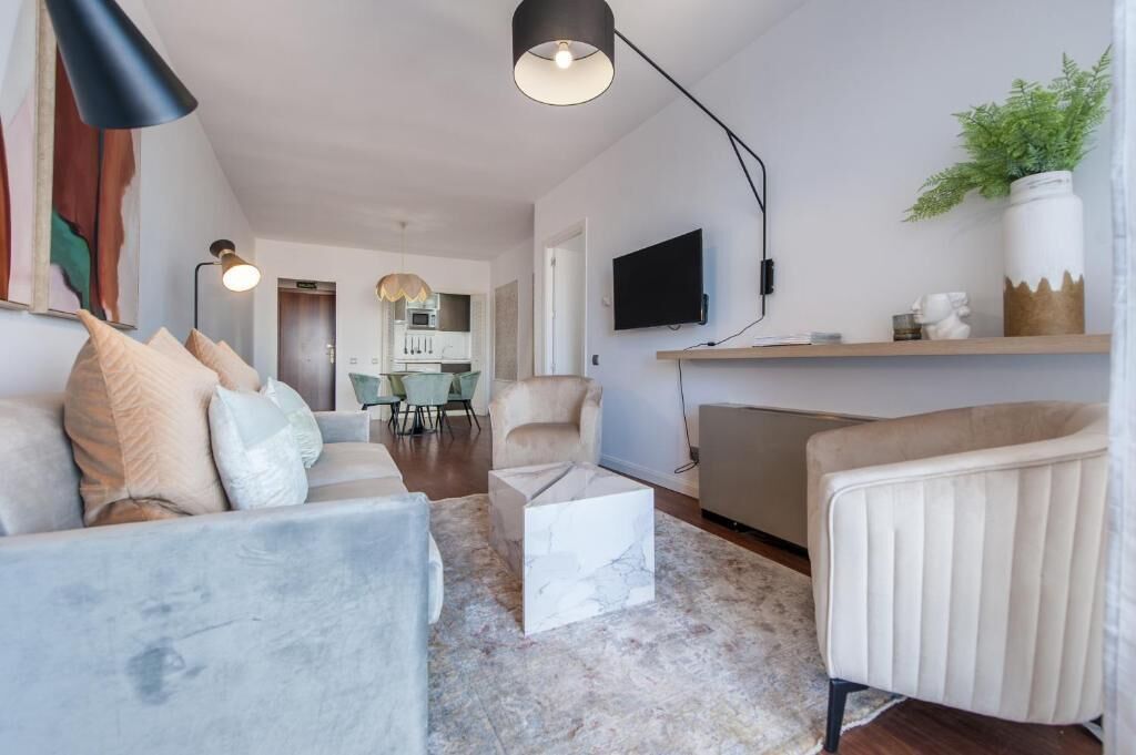 Una sala de estar con sofá, sillón, mesa de centro y televisión en la pared.