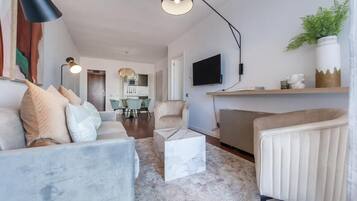 Una sala de estar con sofá, sillón, mesa de centro y televisión en la pared.
