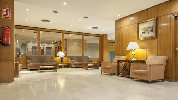 A hotel lobby with a reception desk, seating area, and a fire extinguisher. - La Castellana - Plaza Catilla III (Madrid)