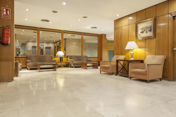 Un vestíbulo de hotel con mostrador de recepción, zona de estar y extintor.