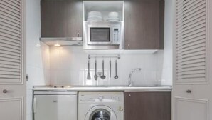 A compact kitchen with a washing machine, microwave, and utensils hanging on the wall. - La Castellana - Plaza Catilla III (Madrid)