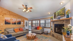 A living room with a fireplace, wooden walls, and a ceiling fan. - Coyote Crossing (Sevierville)