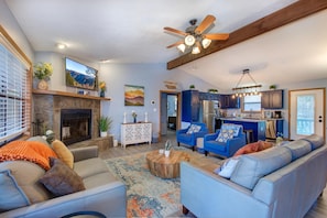 A living room with a fireplace, a ceiling fan, and a kitchen area with blue cabinets. - Coyote Crossing (Sevierville)