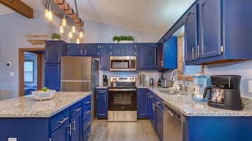 Una cocina con gabinetes azules, electrodomésticos de acero inoxidable, encimeras de granito e iluminación colgante.