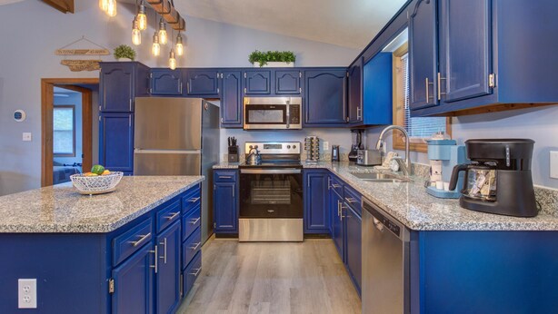 A kitchen with blue cabinets, stainless steel appliances, granite countertops, and pendant lighting. - Coyote Crossing (Sevierville)