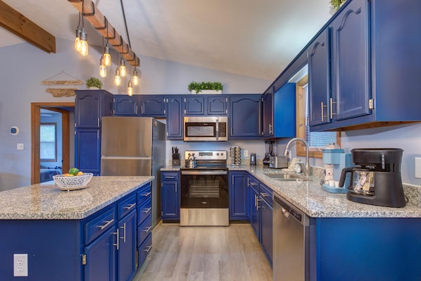 A kitchen with blue cabinets, stainless steel appliances, granite countertops, and pendant lighting. - Coyote Crossing (Sevierville)