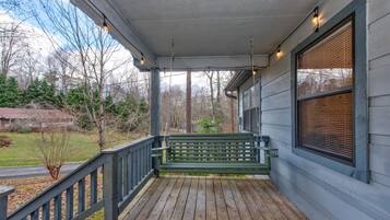 A wooden porch with a bench, a railing, and a window with blinds.