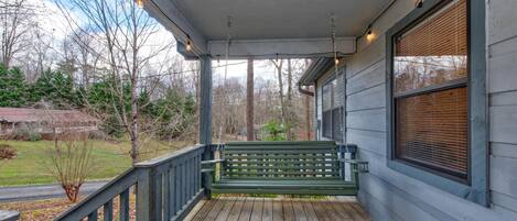 A wooden porch with a bench, a railing, and a window with blinds.