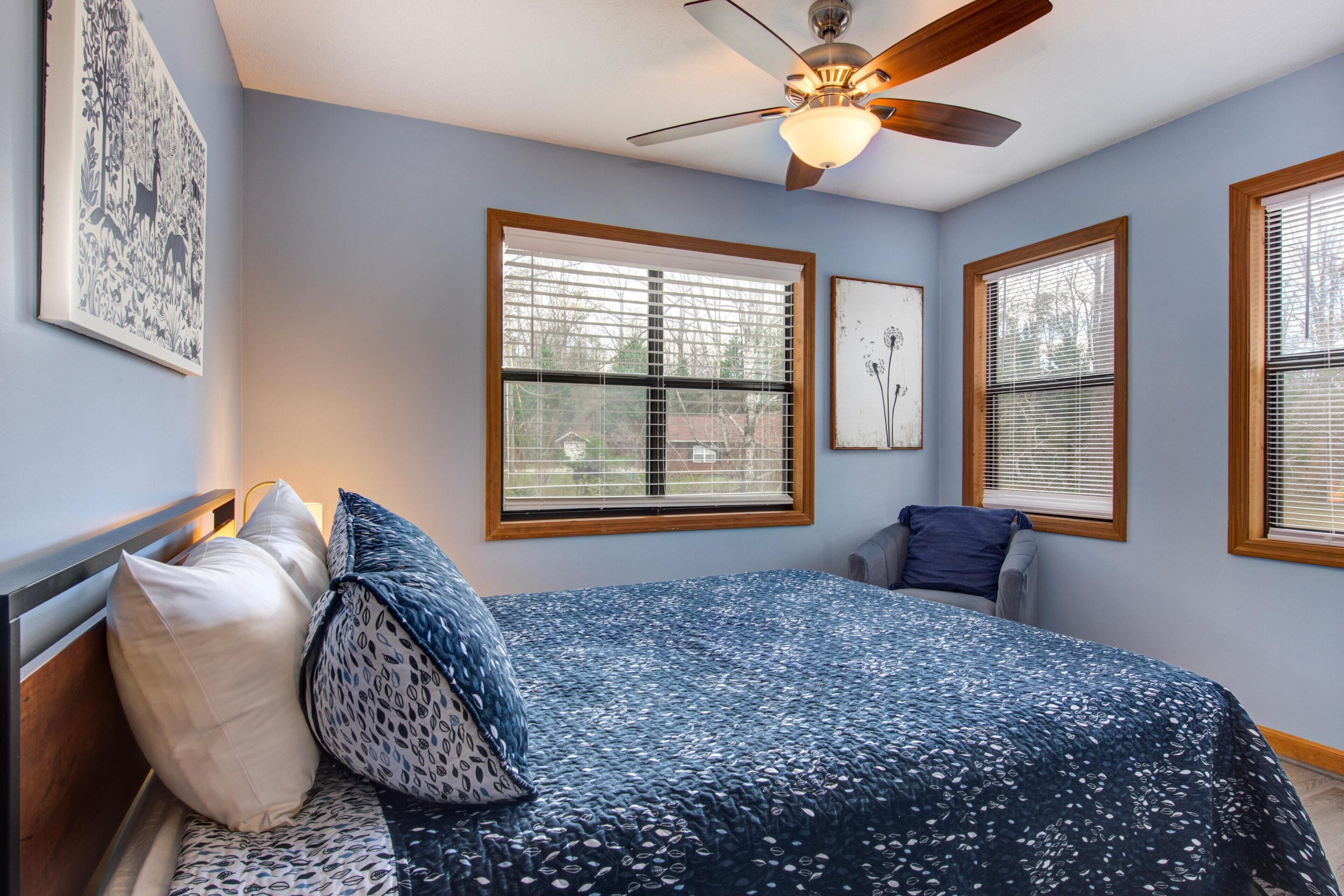A bedroom with a bed, a ceiling fan, and three windows with blinds.