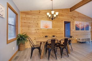 A wooden interior with a dining table, chairs, a chandelier, and artwork on the walls. - Coyote Crossing (Sevierville)