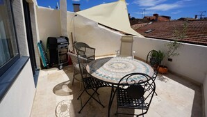 Una terrazza sul tetto con un tavolo rotondo e sedie, un barbecue e una pianta in vaso.