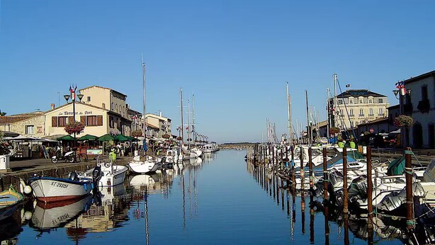 Una marina con barche ormeggiate lungo l'acqua, edifici a sinistra e cielo sereno.