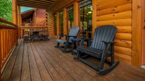 Eine Holzterrasse mit Adirondack-Stühlen, einem überdachten Sitzbereich und Blick ins Innere.