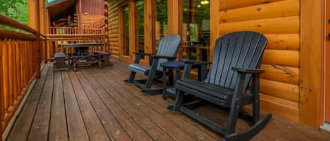 A wooden deck with Adirondack chairs, a covered seating area, and a view of the interior.