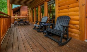 Une terrasse en bois avec des fauteuils Adirondack, un espace salon couvert et une vue sur l’intérieur.
