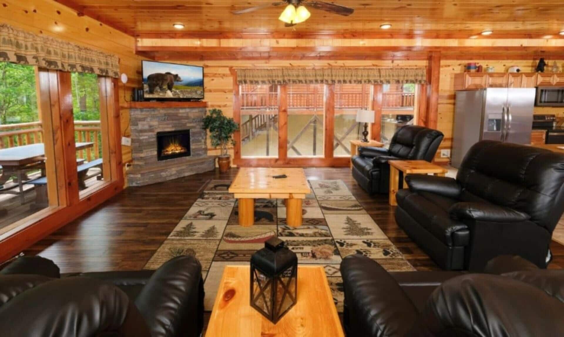 A cozy cabin interior with a stone fireplace, leather furniture, and a television mounted on the wall.
