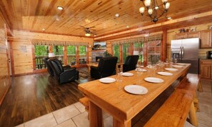 A wooden cabin interior with a dining table set for six, a fireplace, and a kitchen area. - Emerald and Evergreen at Sherwood (Pigeon Forge)