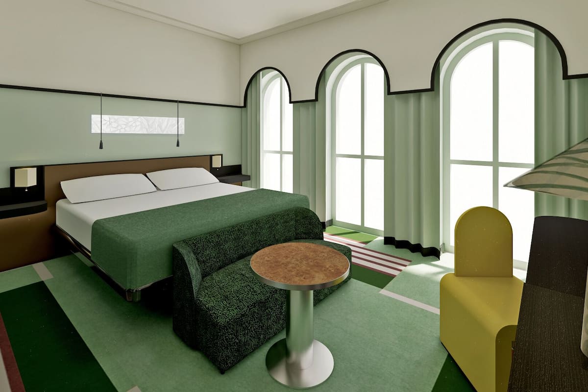 Une chambre d’hôtel avec un lit, une table ronde, un fauteuil jaune et de grandes fenêtres en arc de cercle.