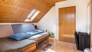 Een gezellige kamer met een schuine kap, een bed met een deken met blauw patroon, een houten deur en een klein raam.