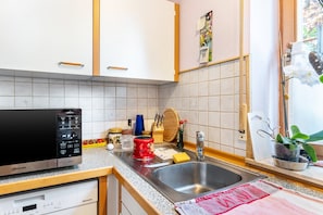 Een keuken met een ingebouwde magnetron, een spoelbak en diverse keukenspullen op het aanrecht.