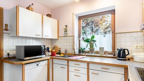 Een keuken met witte kastjes, een magnetron, een spoelbak en een raam met uitzicht op bomen.