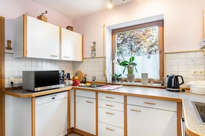 Una cocina con alacenas blancas, microondas, fregadero y ventana con vista a árboles.