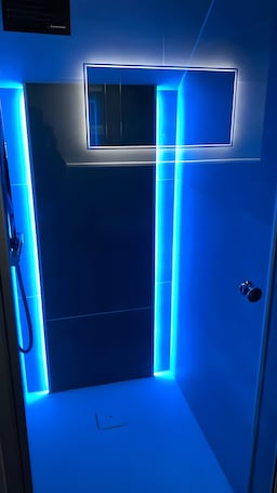A modern bathroom with blue LED lighting, a shower area, and a visible hand dryer.. Work&Travel Pension Tobias – Ideal for Contractors, Tradespeople & Travelers – Welcome!