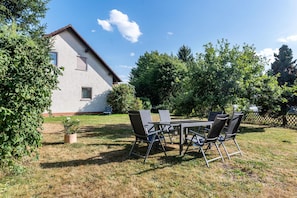 A patio area with a table and chairs, a small potted plant, and a house in the background.