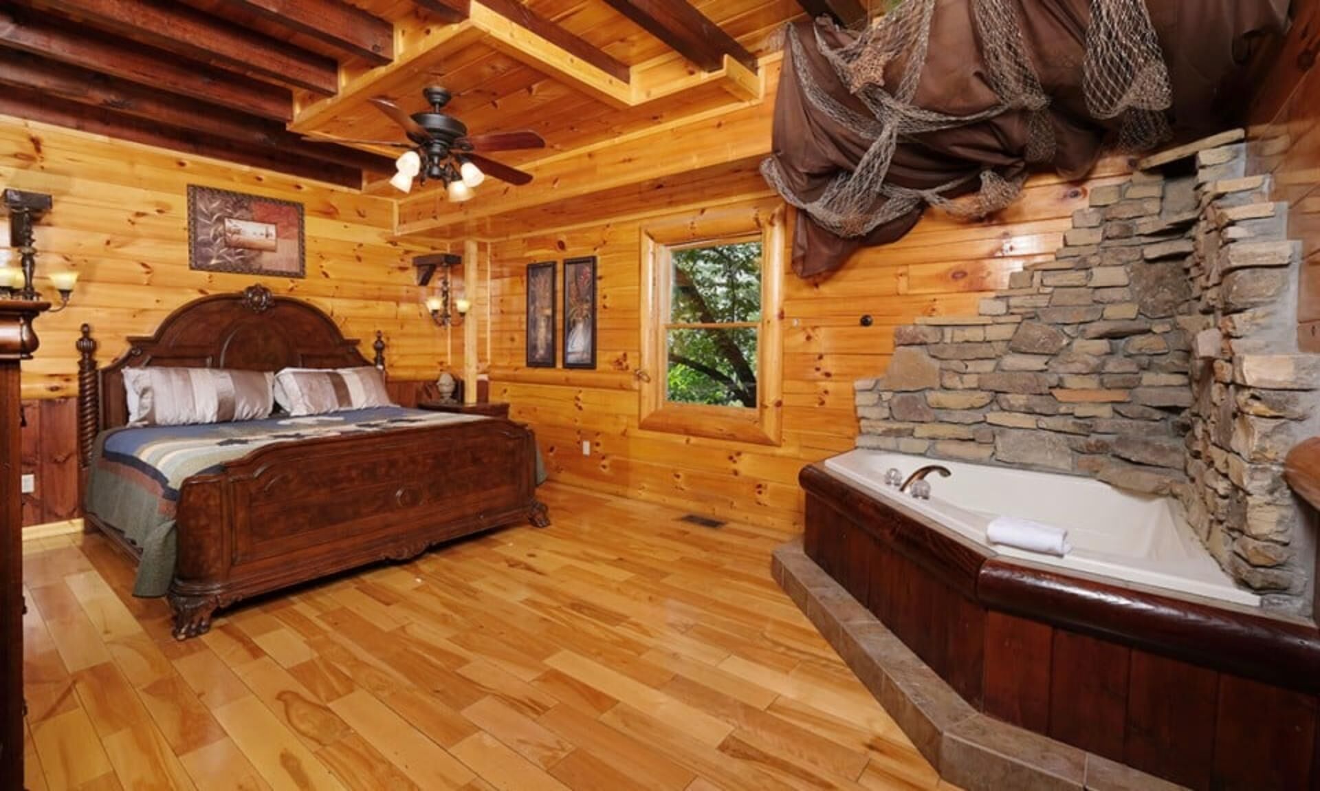 A wooden cabin bedroom with a bed, a stone wall, a window, and a ceiling fan.