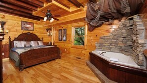 Ein Schlafzimmer einer Holzhütte mit einem Bett, einer Steinwand, einem Fenster und einem Deckenventilator.