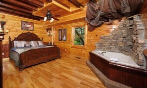 A wooden cabin bedroom with a bed, a stone wall, a window, and a ceiling fan. - Splash N Around (Sevierville)