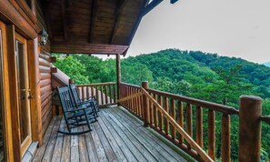 Eine Holzterrasse mit einem Schaukelstuhl und Blick auf einen bewaldeten Berg.